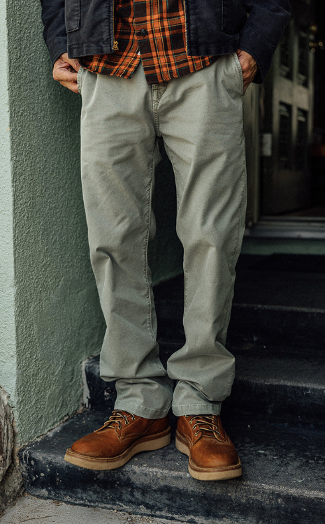 Person wearing a plaid shirt, beige pants, and brown shoes standing on steps.