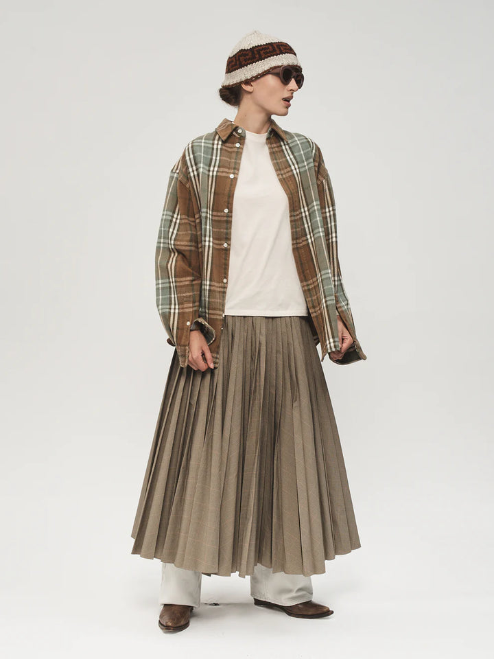 Person wearing a plaid shirt, white top, pleated skirt, and brown shoes on a white background