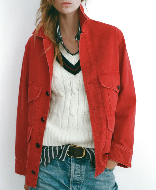 Person wearing a red jacket over a white sweater with a striped shirt underneath, on a plain background.