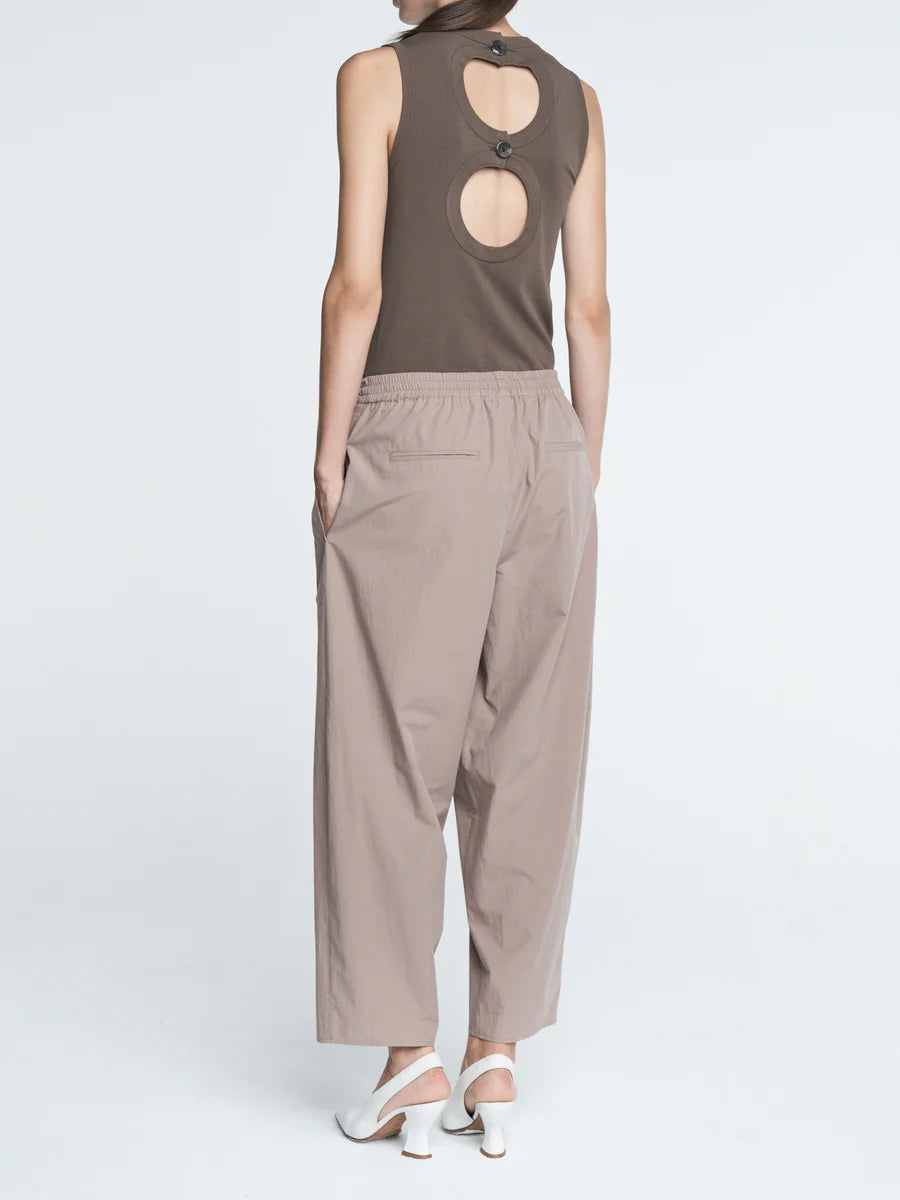 Person wearing a sleeveless brown top and beige pants on a white background