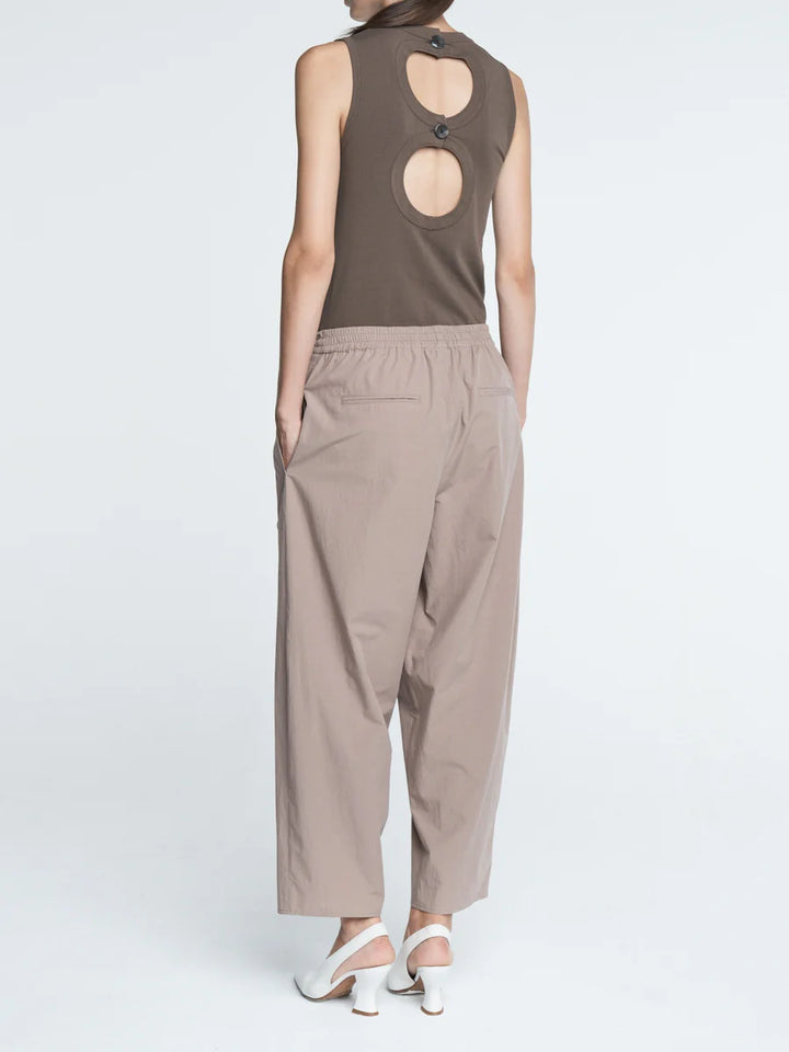 Person wearing a sleeveless brown top and beige pants on a white background