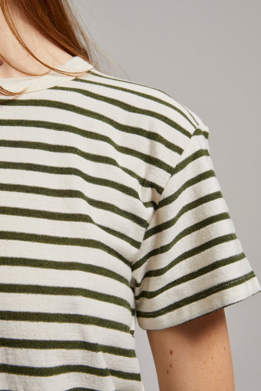 Person wearing a striped shirt with green and white horizontal stripes on a plain background