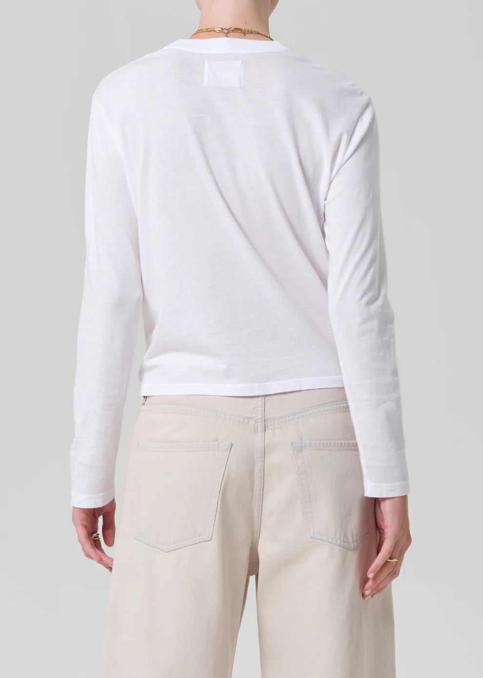 Person wearing a white long-sleeve shirt and beige pants on a light gray background