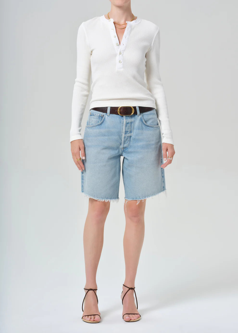 Person wearing a white long-sleeve shirt and light blue denim shorts on a plain background