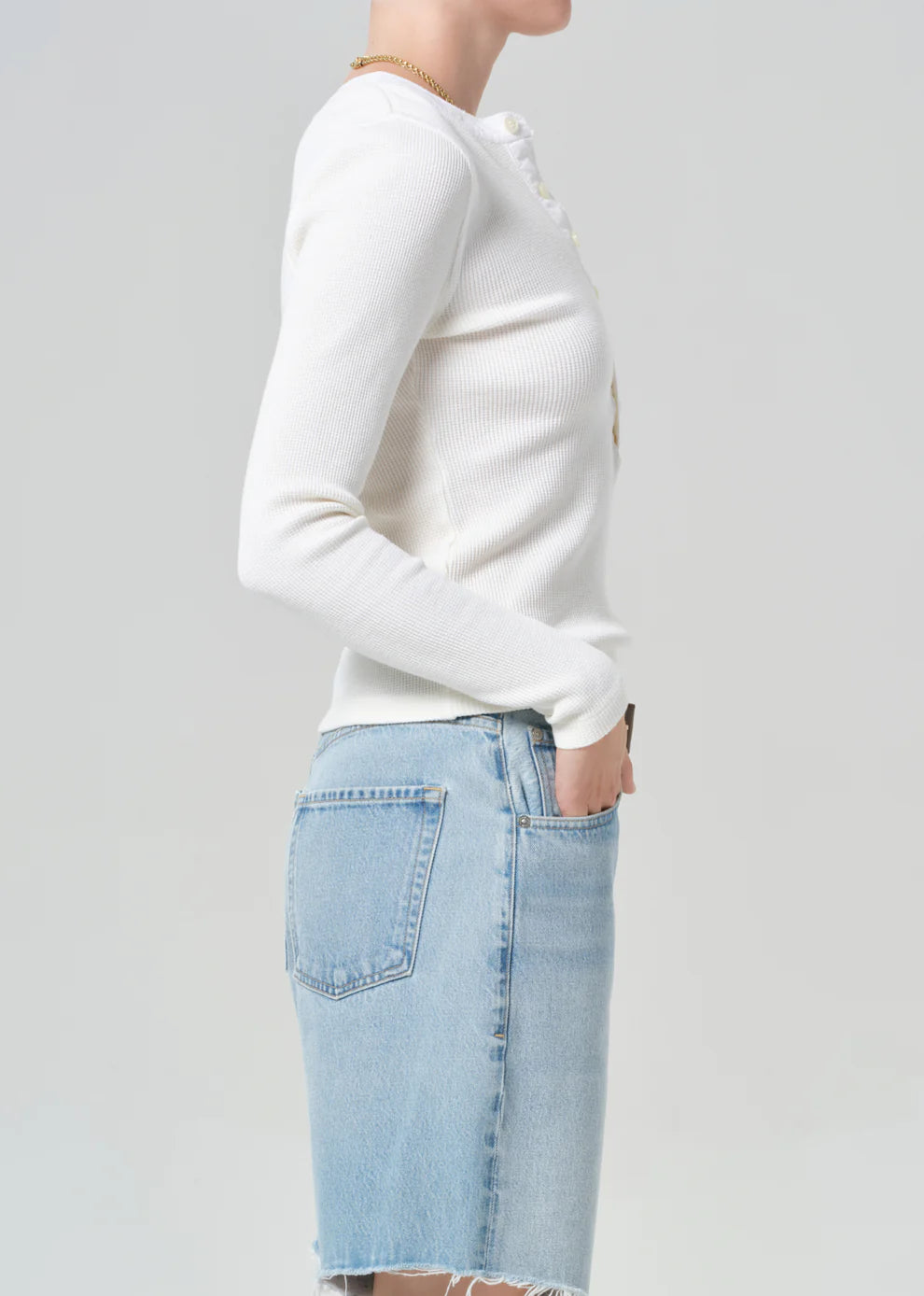 Person wearing a white long-sleeve shirt and light blue denim skirt on a plain background