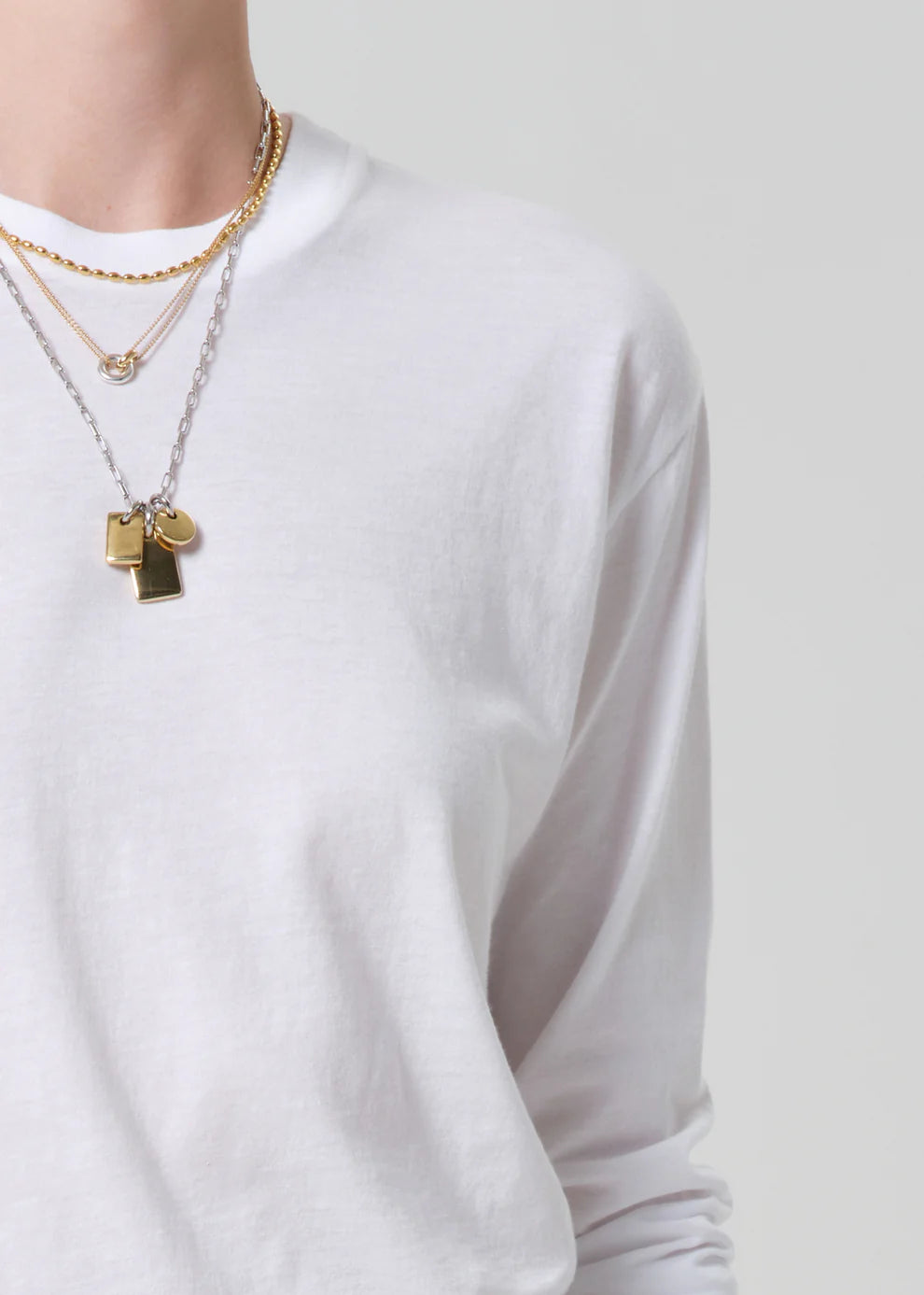 Person wearing a white long-sleeve shirt with layered gold necklaces on a plain background