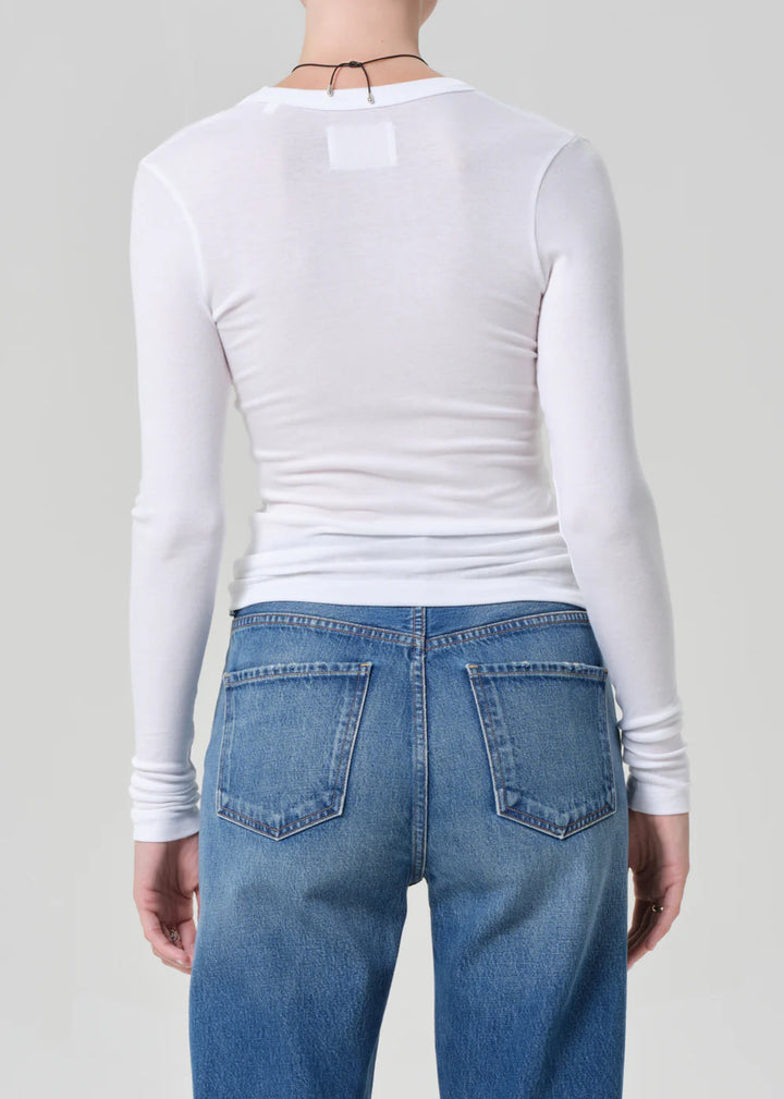 Person wearing a white long-sleeve top and blue jeans on a plain background