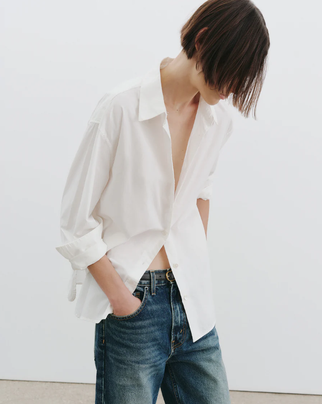 Person wearing a white open-neck shirt and blue jeans against a white background