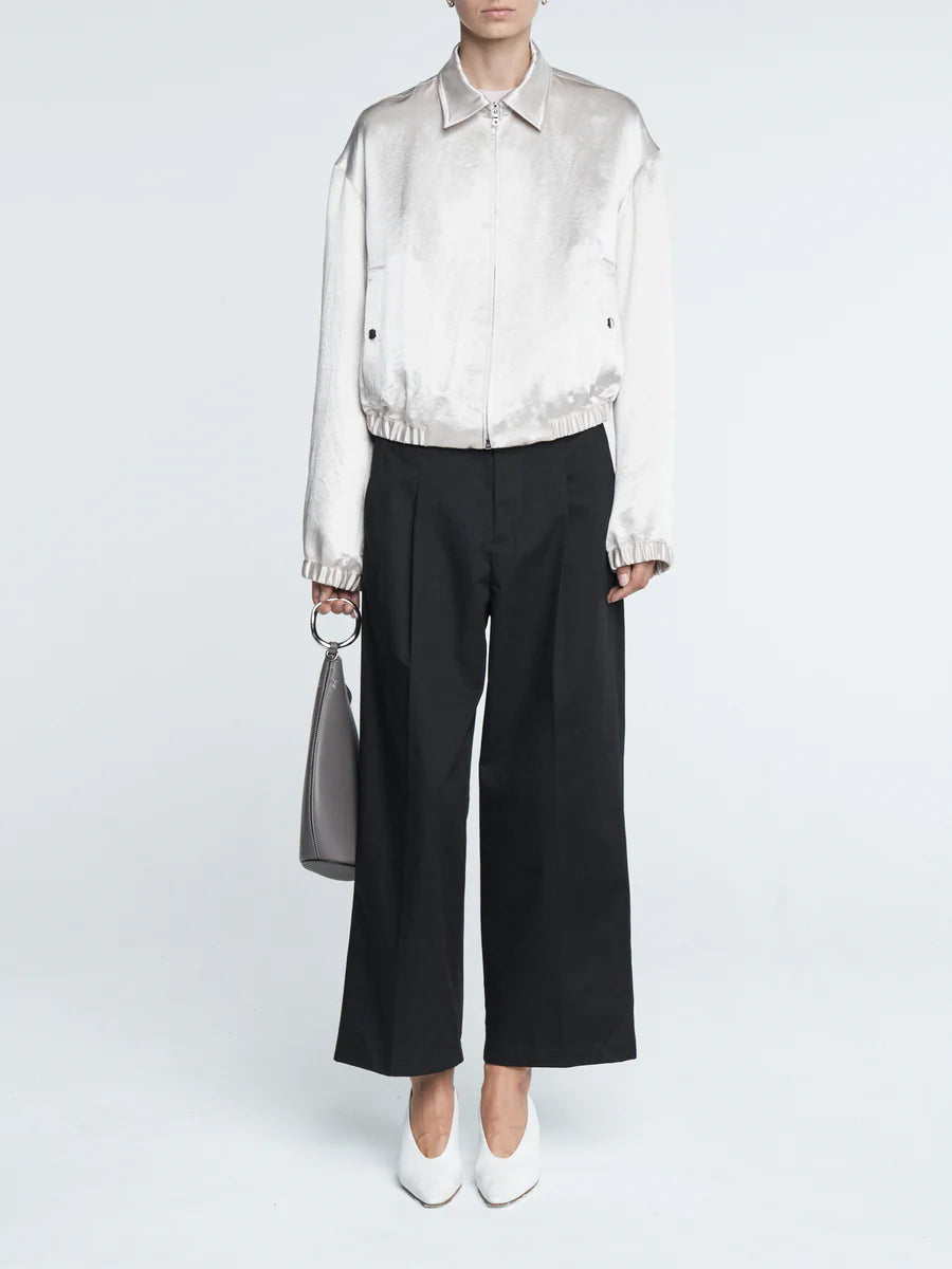 Person wearing a white satin shirt and black wide-leg pants holding a gray handbag on a white background