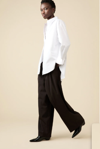 Person wearing a white shirt and brown pants on a beige background