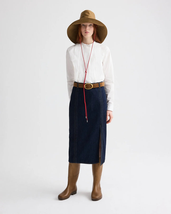 Person wearing a white shirt, navy skirt, brown boots, and wide-brimmed hat on a white background