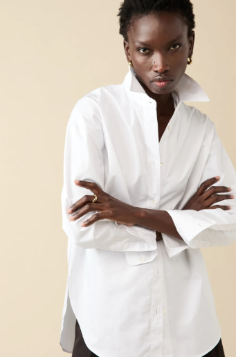 Person wearing a white shirt with arms crossed against a beige background