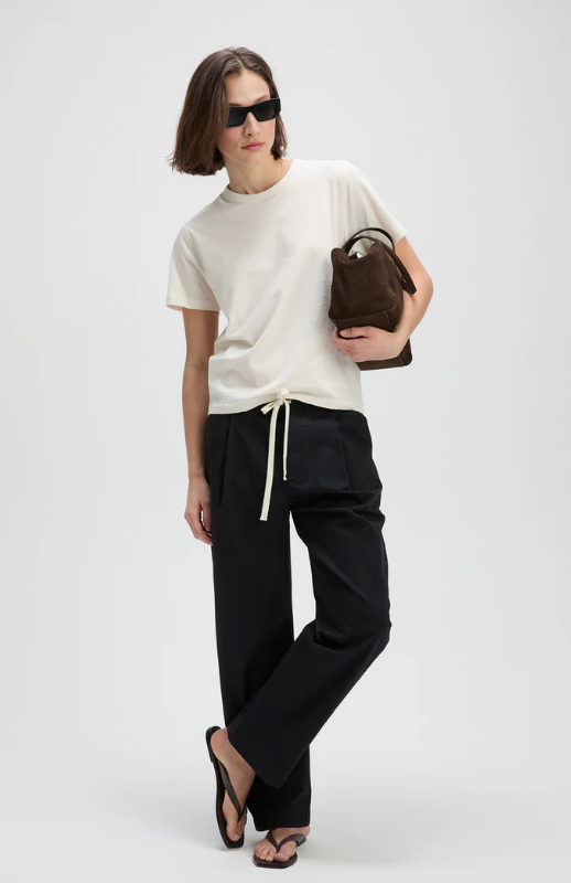 Person wearing a white t-shirt and black pants, holding a brown bag on a white background