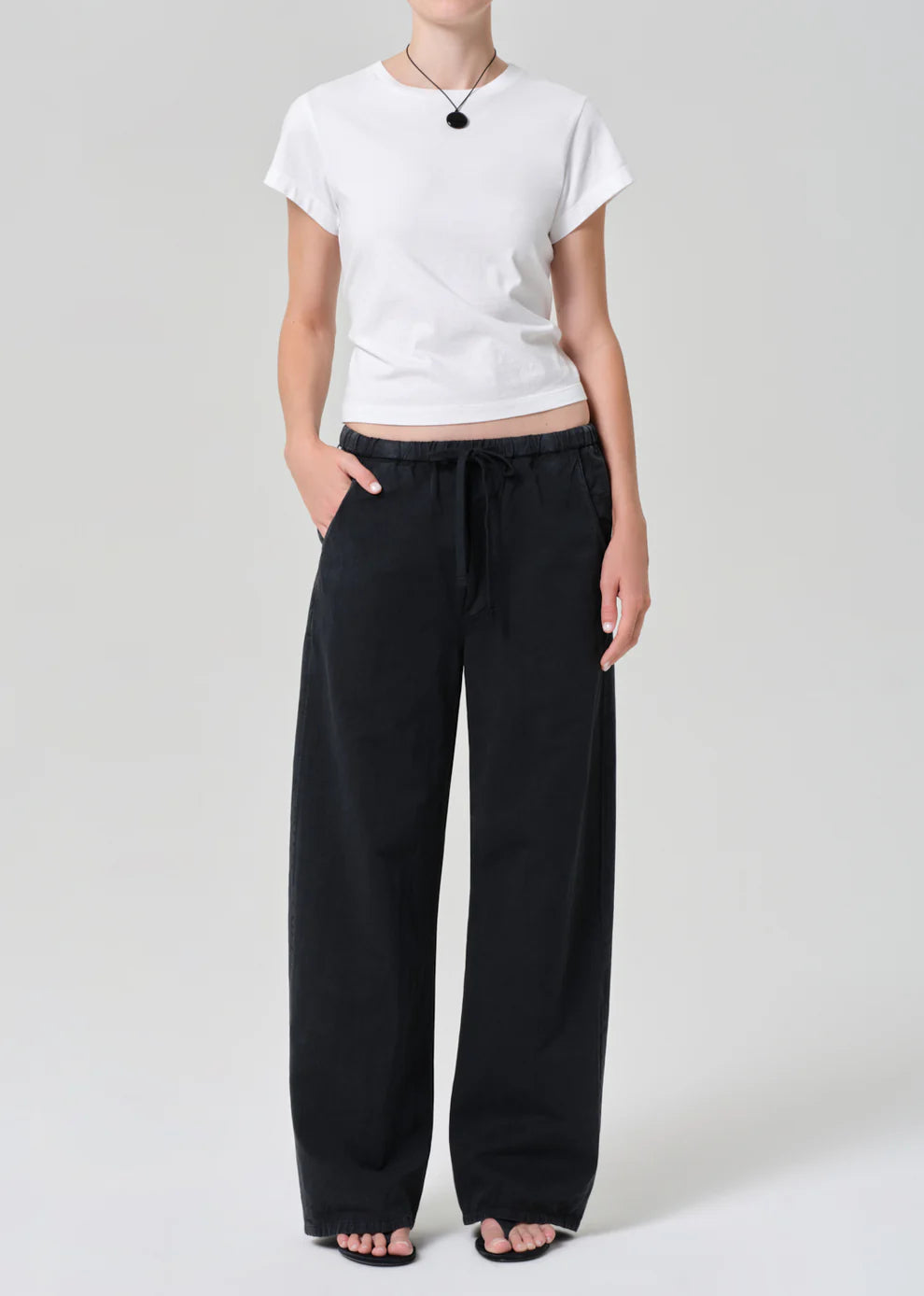 Person wearing a white t-shirt and black pants on a plain background