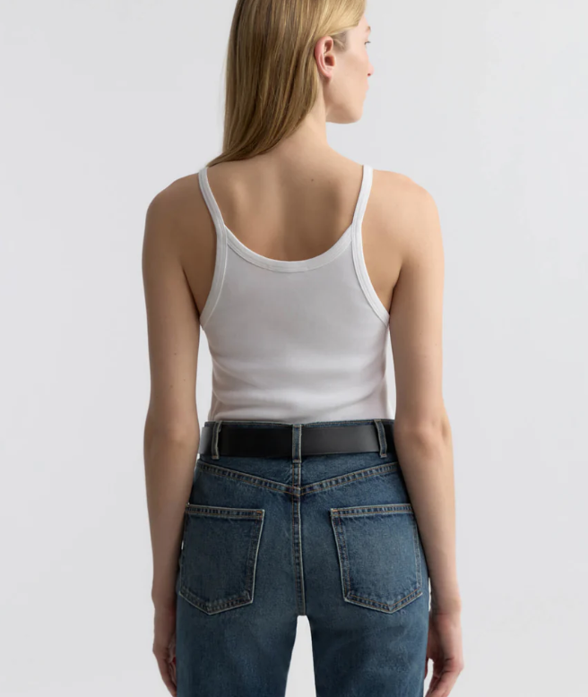Person wearing a white tank top and blue jeans on a plain background