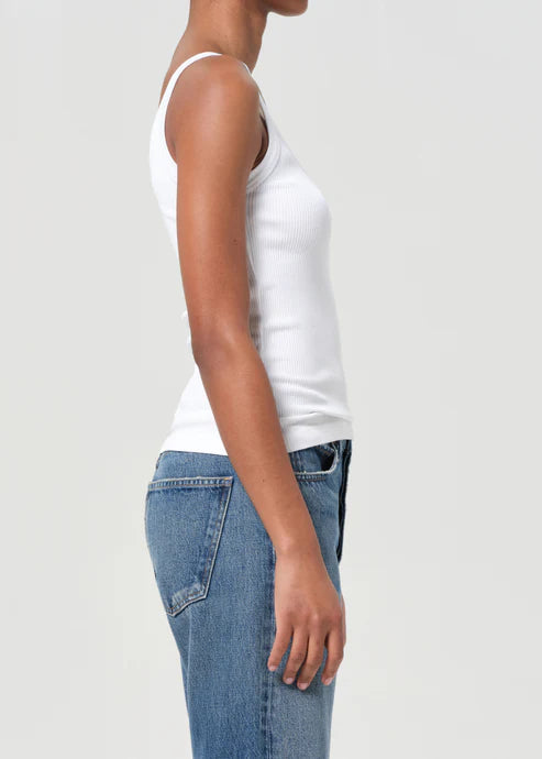 Person wearing a white tank top and blue jeans on a plain background