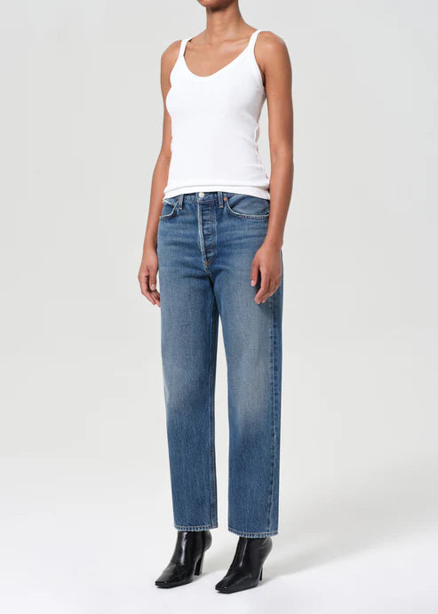 Person wearing a white tank top and blue jeans on a white background