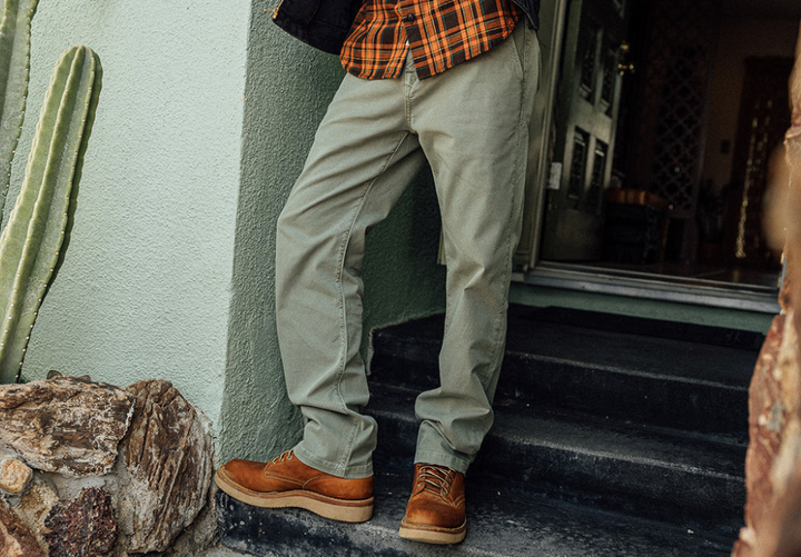 Person wearing beige pants and brown shoes standing on steps next to a cactus plant.