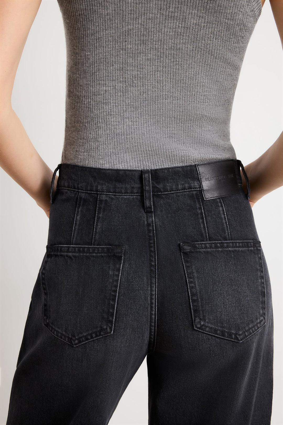 Person wearing black high-waisted jeans and a gray ribbed top on a light gray background