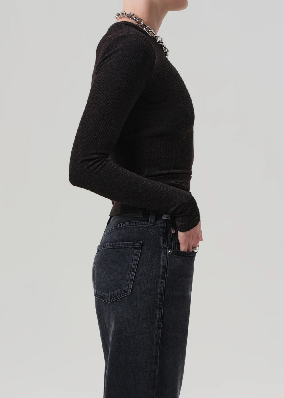 Person wearing a black long-sleeve top and dark jeans on a light gray background