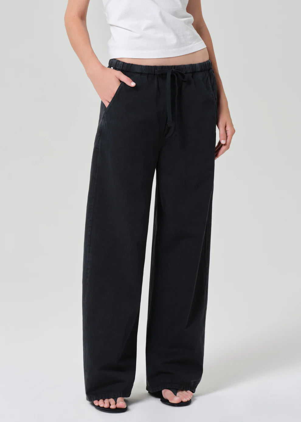 Person wearing black wide-leg pants and a white top on a light gray background