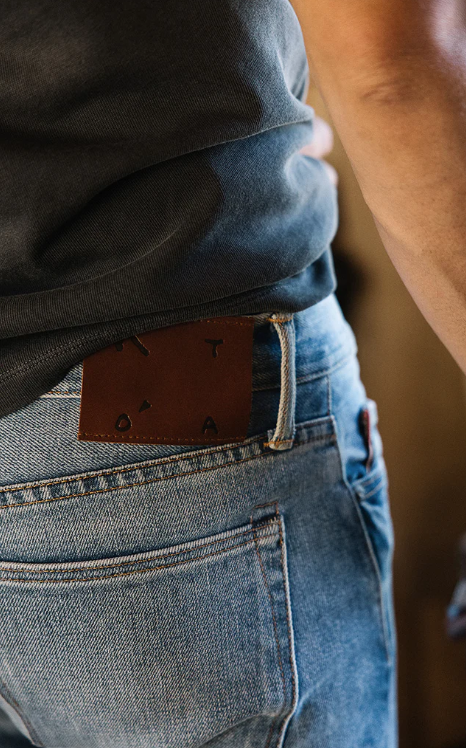 Person wearing blue jeans with a brown leather belt featuring a decorative buckle.