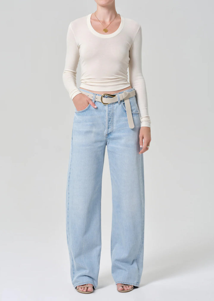 Person wearing light blue jeans and a cream long-sleeve top on a white background