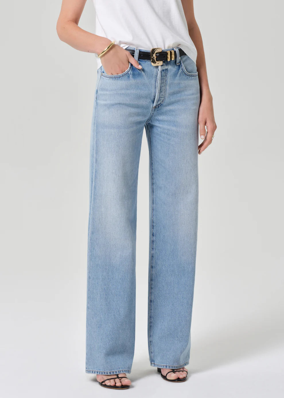 Person wearing light blue jeans and a white top on a plain background