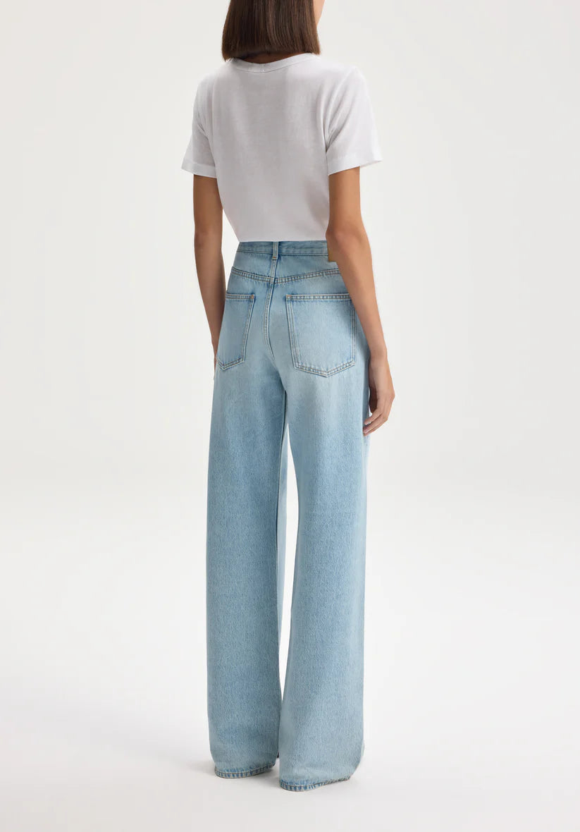 Person wearing light blue jeans and a white top on a plain background