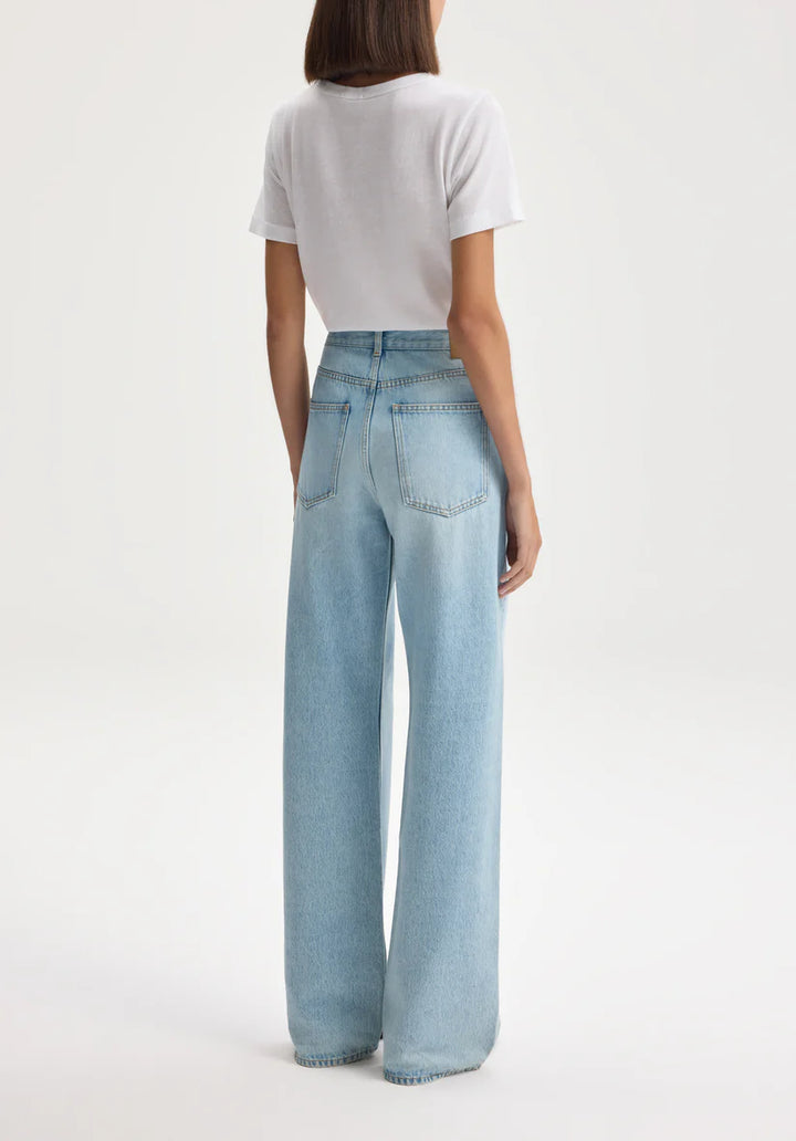 Person wearing light blue jeans and a white top on a plain background