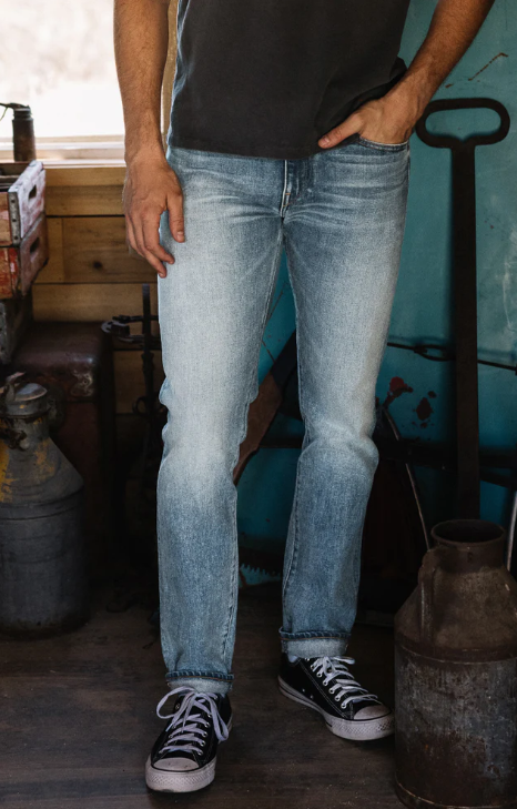 Person wearing light blue jeans and black sneakers in a workshop setting