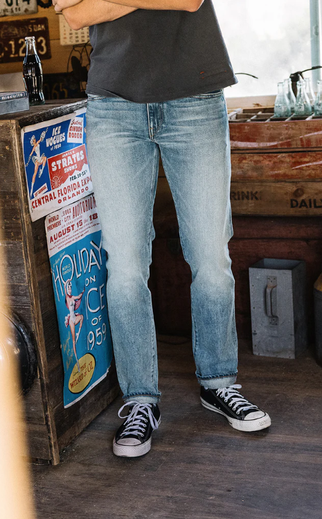 Person wearing light blue jeans and black sneakers standing in front of vintage posters and wooden crates.