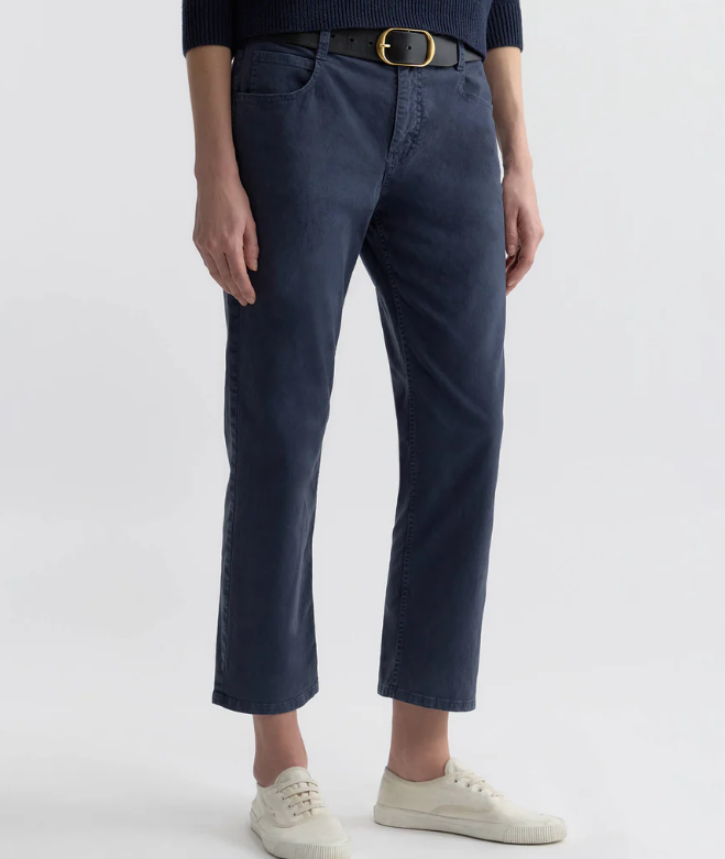 Person wearing navy blue pants with a gold belt on a white background