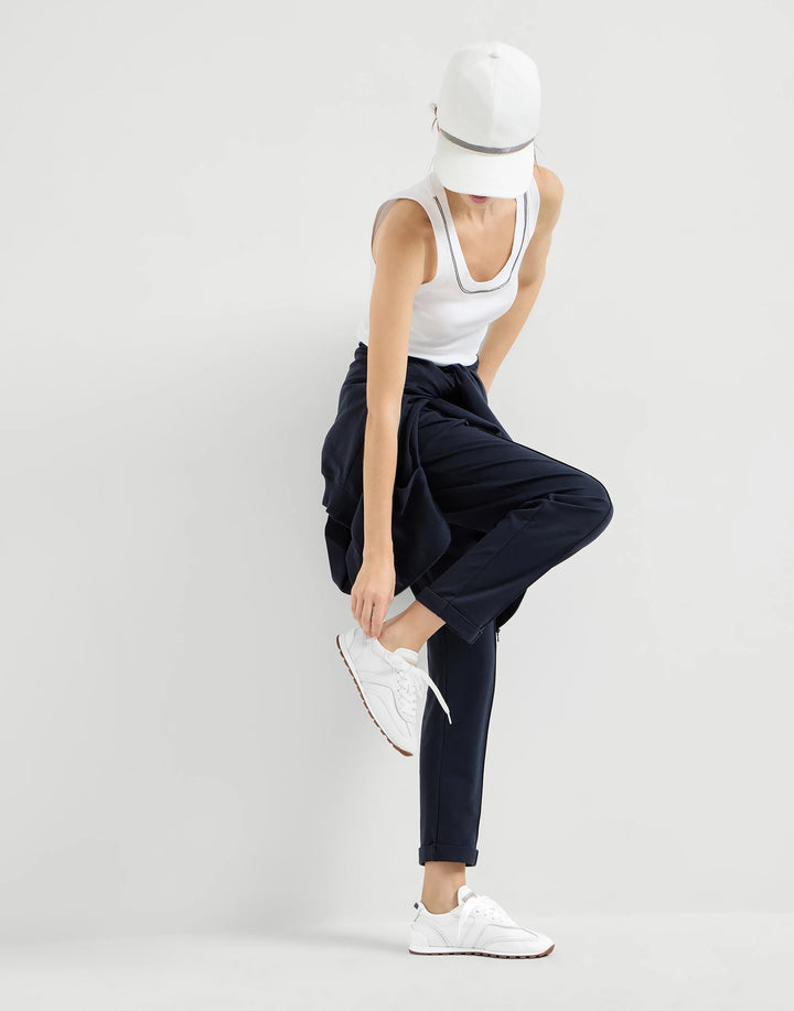 Person wearing navy pants, white tank top, and white sneakers on a light gray background