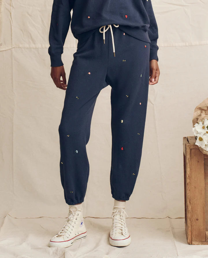 Person wearing navy tracksuit with small colorful embellishments on a neutral background