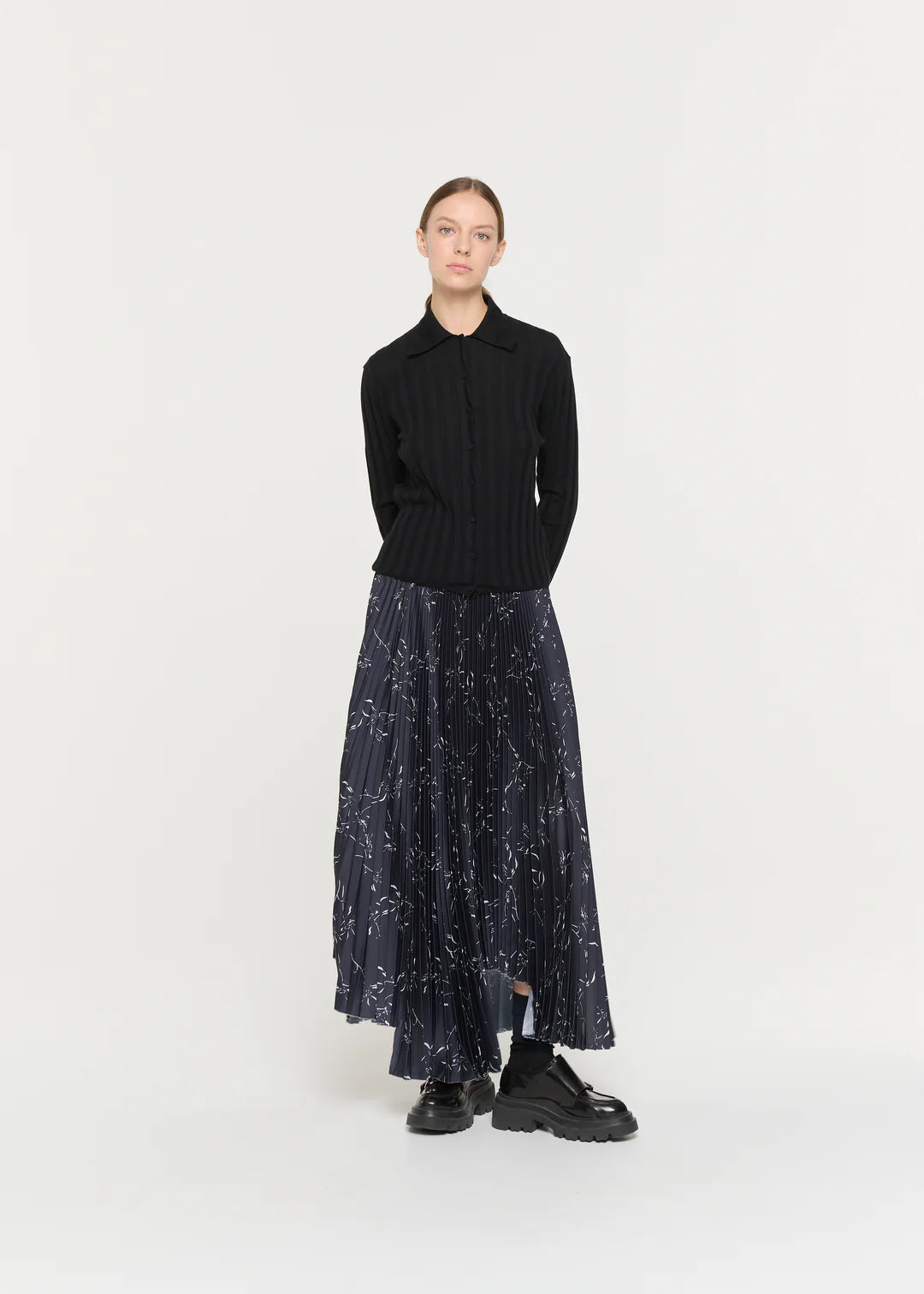 Person wearing a black sweater and patterned skirt on a white background