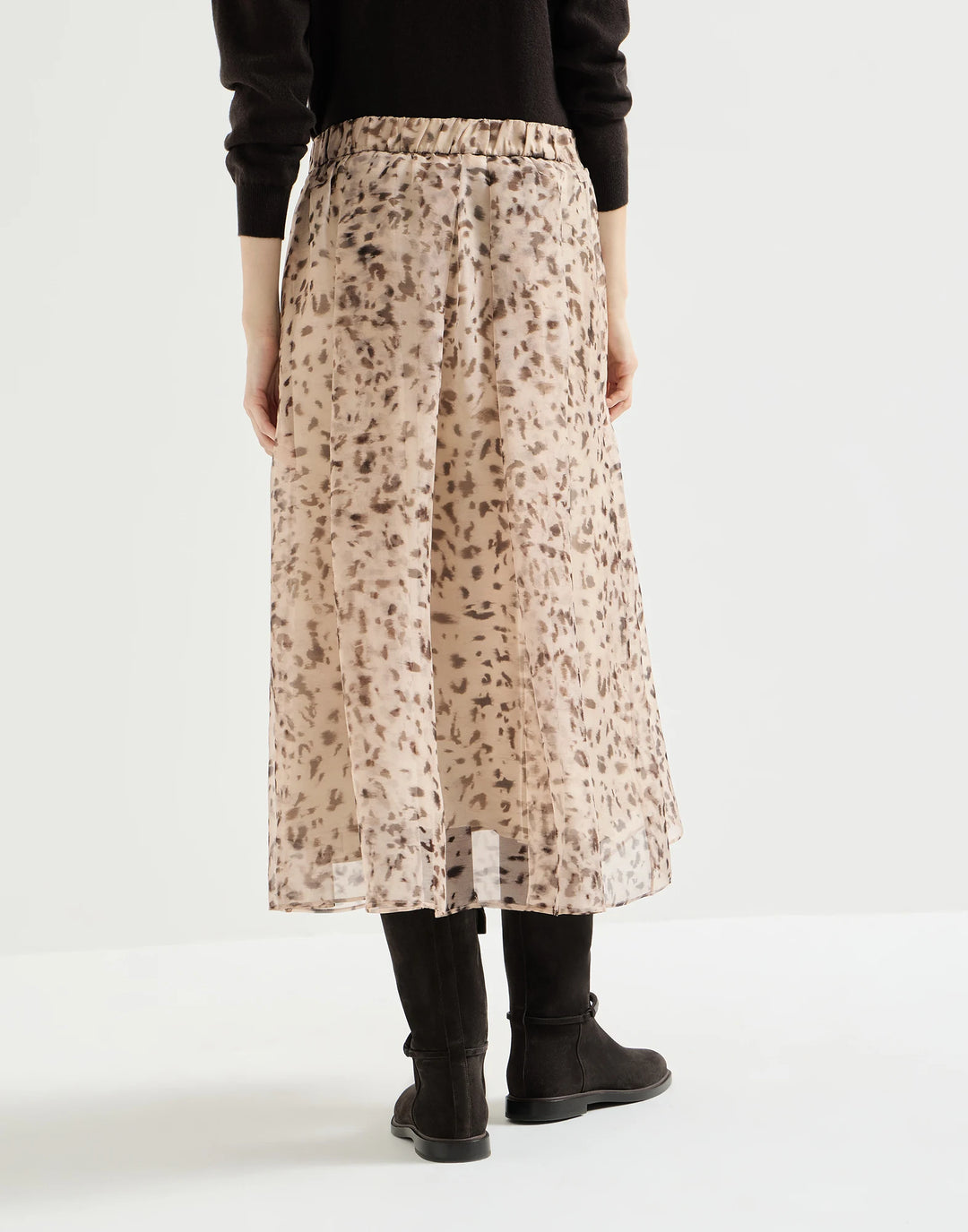 A model shown from the back wearing a beige midi skirt with a brown leopard print, paired with a black long-sleeve top and black boots, against a plain white studio background.