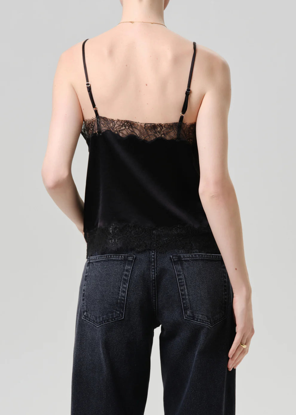 Person wearing a black lace-trimmed top and dark jeans on a plain background