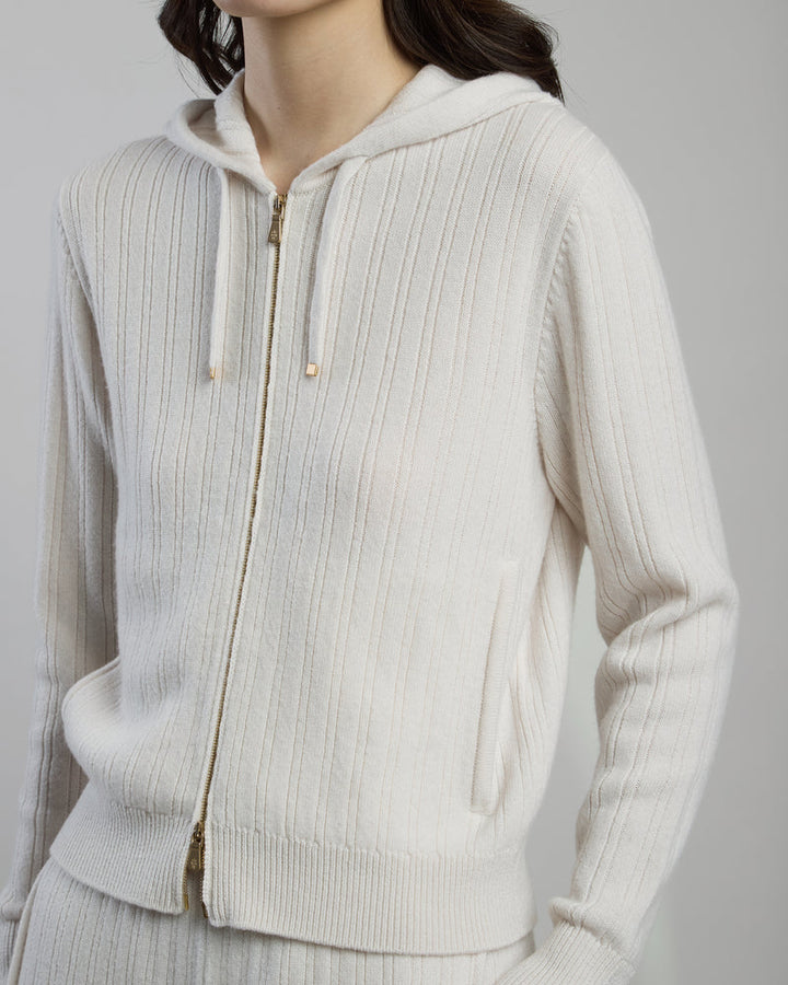 Person wearing a beige ribbed knit hoodie on a gray background