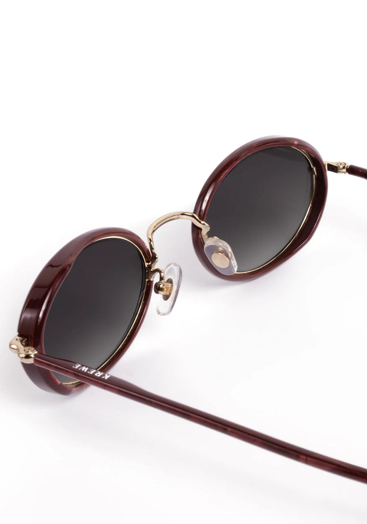 Oval sunglasses with dark brown acetate frames, gold metal rims, and dark lenses, shown on a clean white background.