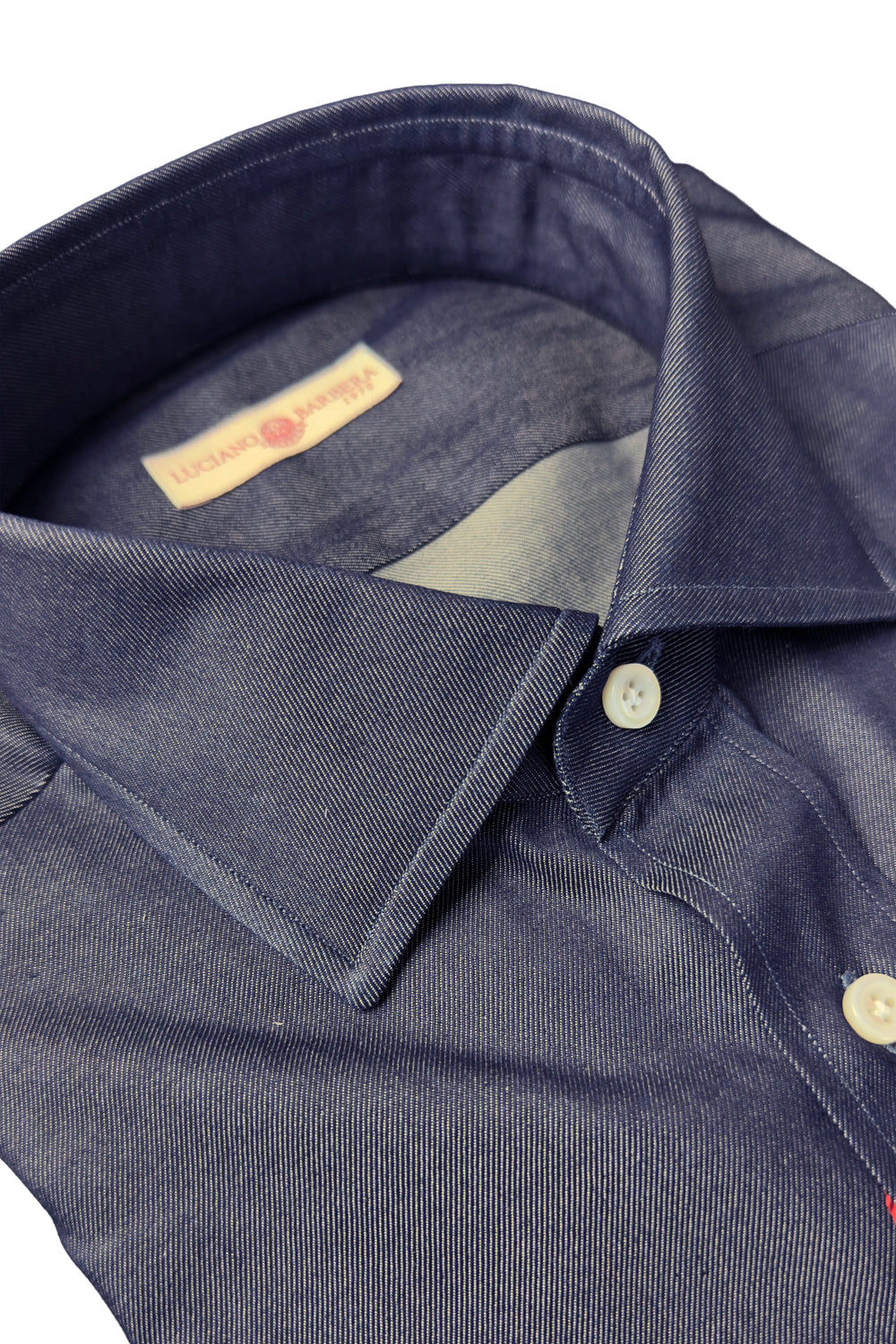 Close-up of a dark navy blue chambray shirt collar with a cream-colored brand label inside the neck and white buttons.