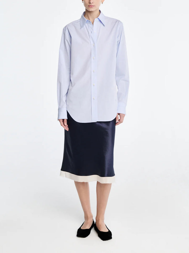 Person wearing a light blue striped shirt and navy satin skirt on a white background