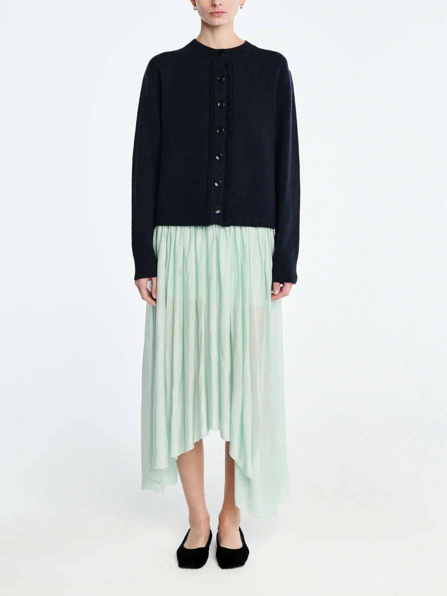 Person wearing a black cardigan and light green pleated skirt on a white background