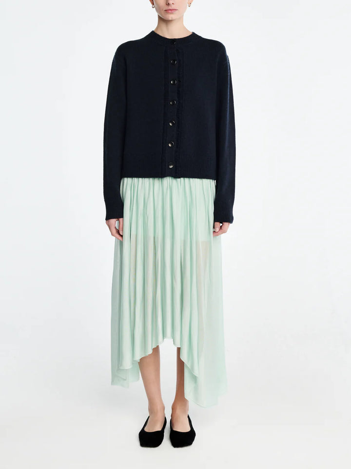 Person wearing a black cardigan and light green pleated skirt on a white background