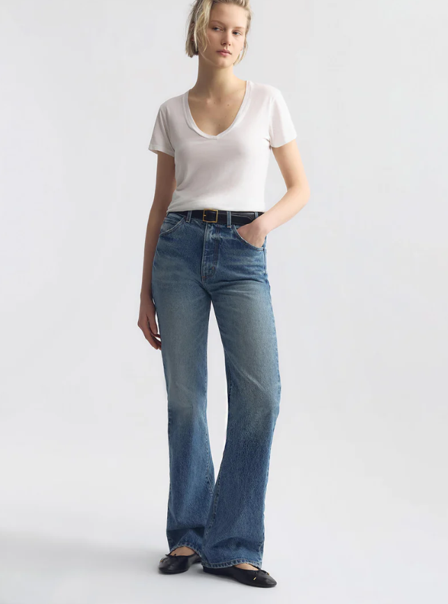 Woman wearing a white t-shirt and blue jeans on a plain background