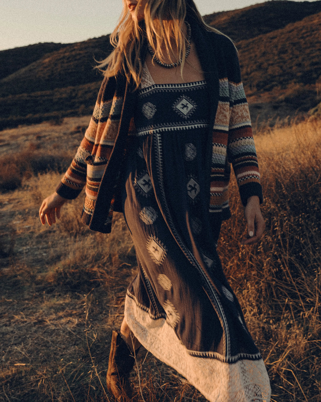 Woman in a patterned dress and cardigan standing in a desert landscape