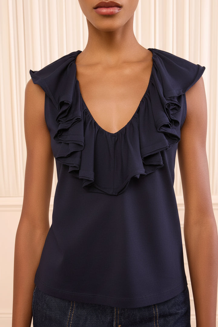 Woman wearing a light-colored blouse with ruffled details against a neutral background