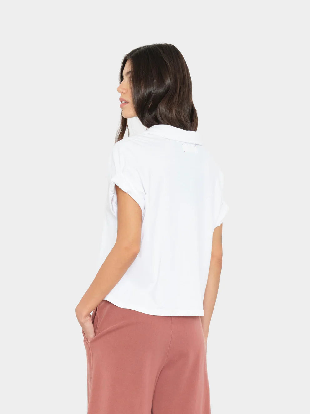 Woman wearing a white top and pink pants on a plain background