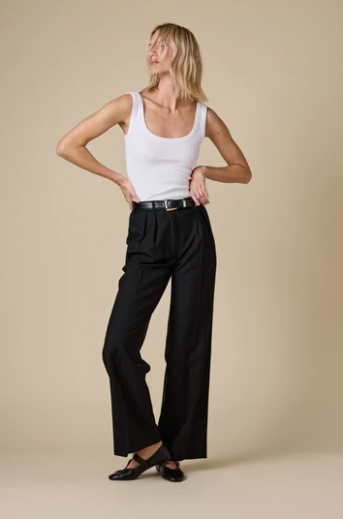 Woman wearing a white tank top and black wide-leg pants on a beige background