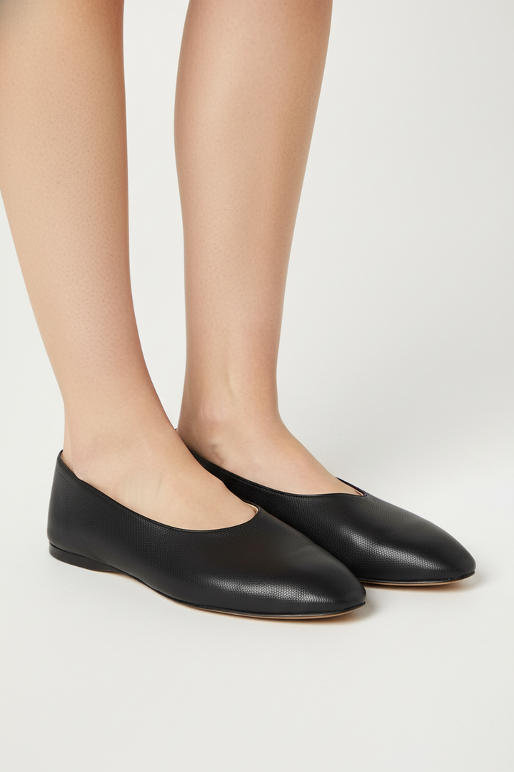 Black flat shoes worn with beige tights on a light gray background